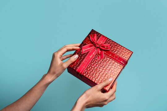 Hands holding red gift box with ribbon on blue background