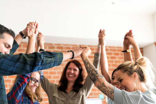 Diverse group of people holding hands in a circle, smiling and celebrating together.