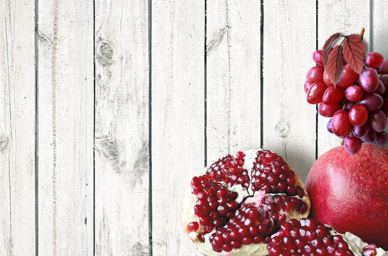 Wooden table top with grapes and pomegranate. Fruits bushes background.