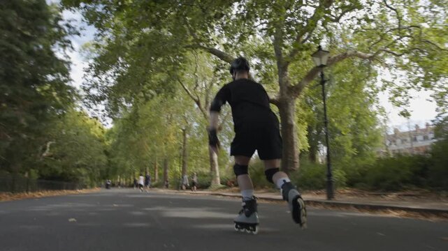 A skater speeds up in Battersea Park, London on a sunny autumn day with his rollerblades