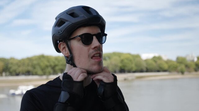 A skater adjusting his helmet near the thames river in battersea park after a long rollerblade session