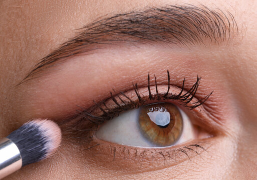 Applying nude eye shadow with makeup brush onto woman's face, closeup