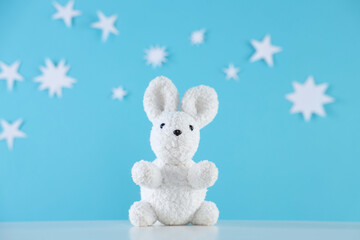 Fototapeta premium One cute toy bunny on white table against light blue background with paper stars