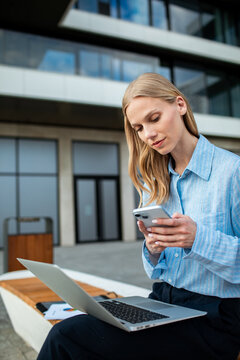 Businesswoman using smartphone and laptop outside office