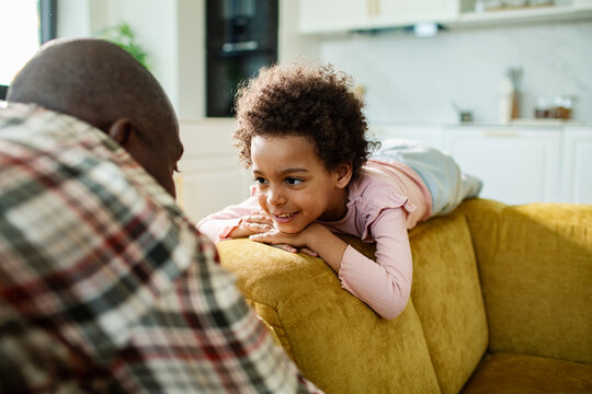 Smiling child chatting with parent on yellow sofa at home