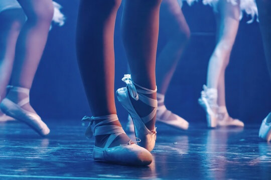 Ballerinas legs and feet wearing pointe shoes during a ballet performance on stage with blue lighting. Capturing discipline and grace