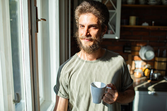 Bearded man enjoying morning coffee by sunny kitchen window