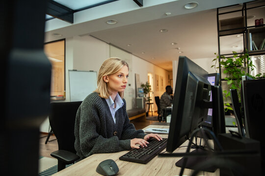 Young businesswoman typing on desktop computer in modern open-plan office