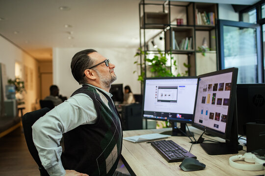 Middle-aged office worker stretching back at computer desk
