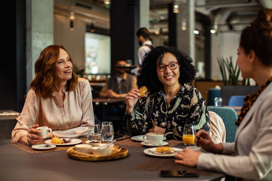 Three female colleagues chatting over breakfast in modern cafe