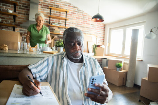 Senior couple planning move with smartphone and paperwork in kitchen