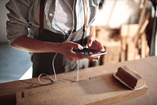 Carpenter using smartphone at workbench in woodshop