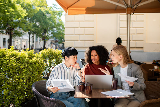 Three businesswomen discussing data at an outdoor cafe