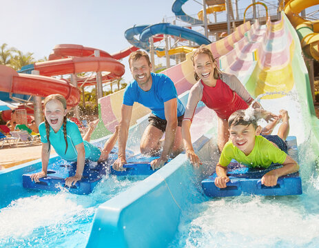 A happy family racing down colorful water slides on mats at a water park.