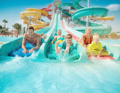 A happy family racing down colorful water slides on mats at a water park.