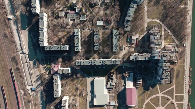 Top-down aerial view drifts over a dense riverside residential district beside railway tracks. Urban planning, transport infrastructure, housing development
