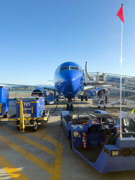 BURBANK, CA, APR 28, 2026: Ground-level view of Southwest Airlines jet nose with air stairs, baggage cart, fire extinguisher, and tow tug in foreground; red flag marker and clear sky, Burbank Airport