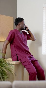 Vertical video: African American man in maroon scrubs in staff room taking incoming call about care