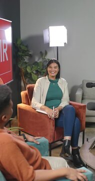 Vertical video: African woman on set holding notebook and pen, laughing as cohost gesturing