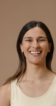 Vertical video: Indian woman in 30s smiling then laughing to lens in studio beige backdrop