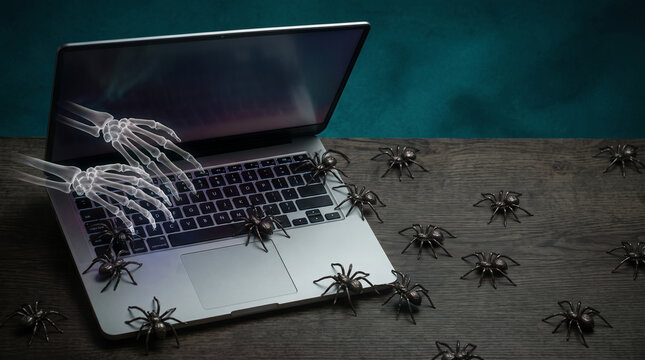 Transparent skeleton hands reaching from a laptop screen, surrounded by spiders on a wooden surface, symbolizing technology fear and digital threats.