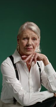 Vertical video: Senior woman making small shifts on chair camera cueing studio pose