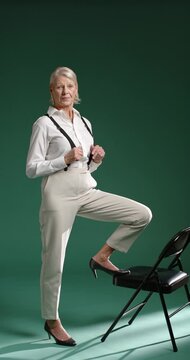 Vertical video: Senior woman starting side with left foot on chair, fixing braces