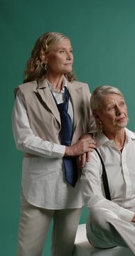 Vertical video: Senior women posing, placing hand and shifting gaze for portrait in teal studio