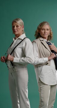Vertical video: Senior female models posing back-to-back, tugging suspenders, smoothing vest in set
