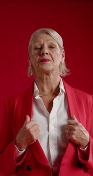 Vertical video: Mature woman posing in studio gripping blazer lapels and adjusting them for camera