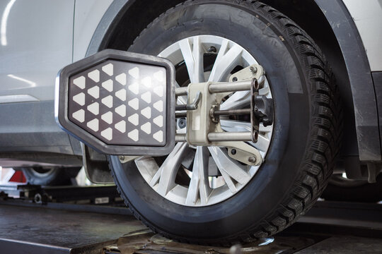Wheel alignment service with sensor target mounted on car wheel, automotive suspension diagnostics, steering geometry adjustment, tire maintenance, repair workshop.