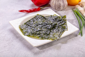 Dark green nori seaweed sheets on white ceramic plate with red pepper, garlic, and green onions in background © Andrei Starostin