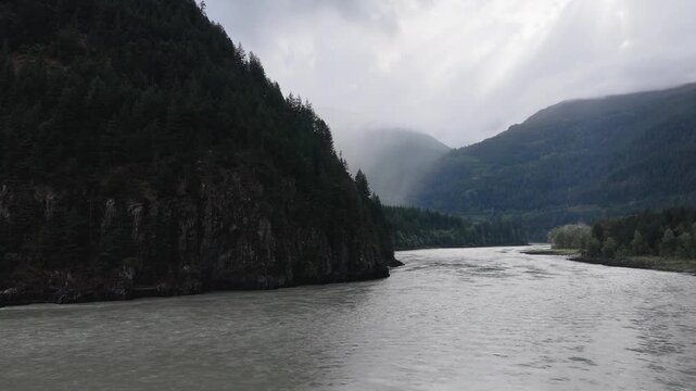 Majestic River Flows Through Lush Forested Mountains Under a Cloudy Sky in British Columbia, Canada