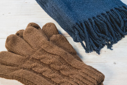 Brown knit gloves and a navy scarf lie together on a whitewashed wood table, a winter set.