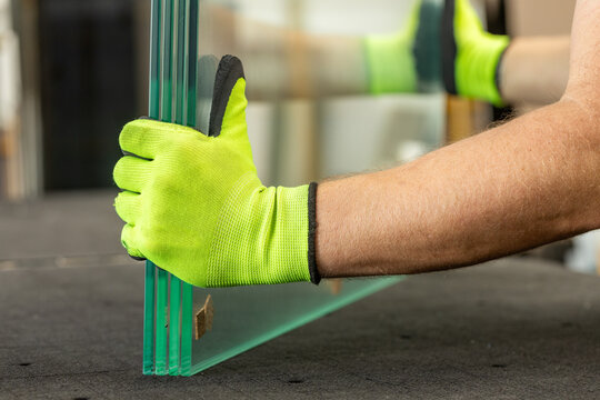 A glazier holds thick, ground, and polished glass sheets. Close-up. A professional workshop specializing in glazing work.