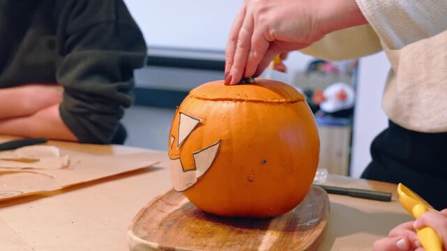 Hands position paper facial shapes on an orange pumpkin to create a jack-o-lantern design, Halloween craft, seasonal pumpkin decoration.