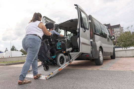 Personal assistant guiding a man with disability up a wheelchair ramp into an adapted van, accessible transportation.