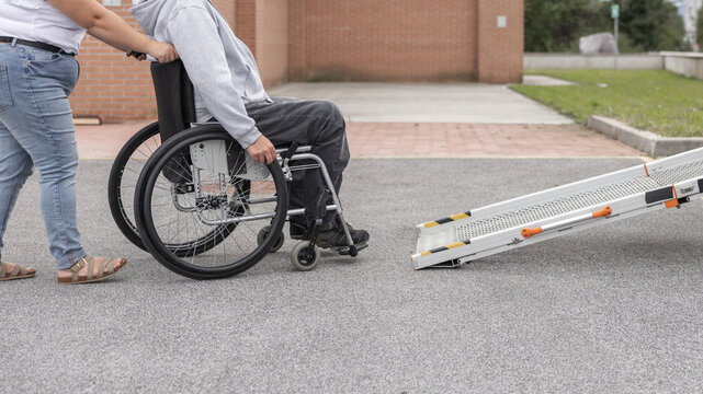 Wheelchair user enjoying an outdoor walk with a Personal assistant and using car ramp. Disability support and social interaction concept.