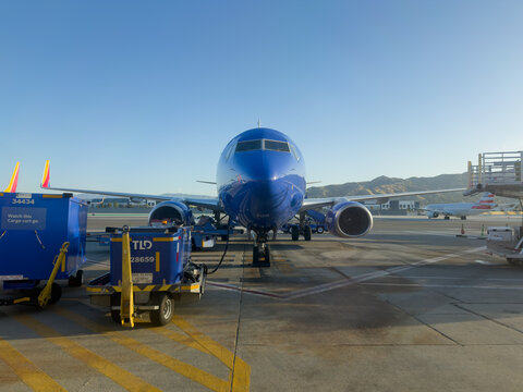 BURBANK, CA, APR 28, 2026: Southwest Airlines Boeing 737 nose-on at Burbank Airport gate with tail fins visible, American Airlines jet taxiing in background, TLD ground carts parked nearby under clear