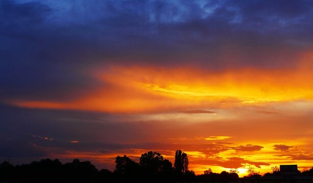 Colorful sunset with dramatic clouds and trees silhouettes with burning sun, colorful sunset landscapes