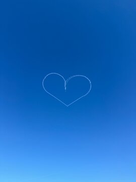 White skywriting smoke forming a heart shape against a bright clear blue sky. Minimal romantic image.