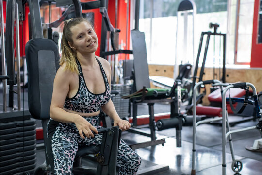 A woman with cerebral palsy exercises on a machine in a gym.