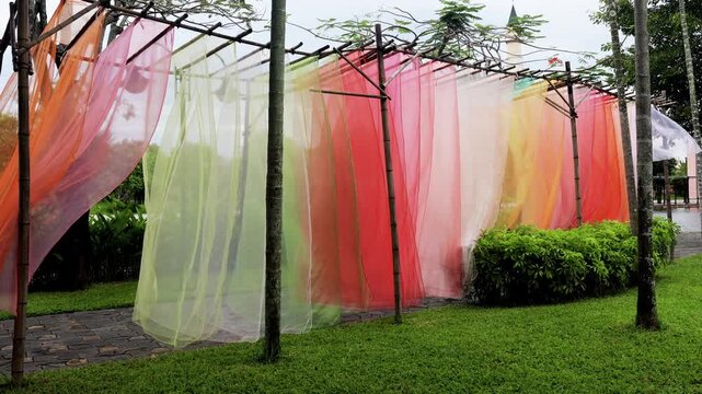 Colorful textile installation in green urban park, where lightweight transparent fabrics create dynamic artistic tunnel and move naturally with breeze, shot handheld. High quality 4k footage