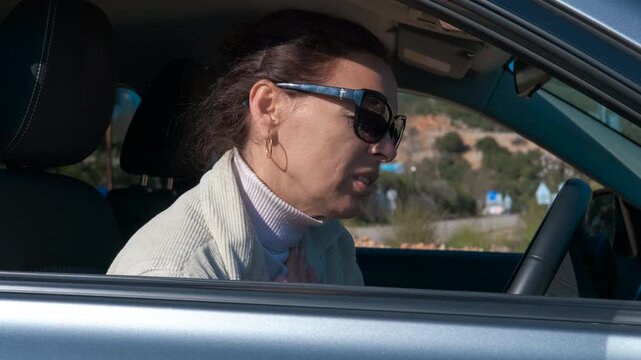 Stressed woman experiencing panic attack in car. Woman in sunglasses sitting inside her car experiencing a sudden panic attack, feeling chest pain and shortness of breath while holding her throat