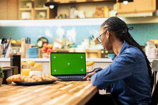 Isolated green screen appears on a laptop with analytics data in the kitchen, combining chroma key and infographic elements with digital tools for teleworking, management and an indoor lifestyle.