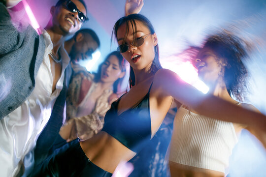 A group of diverse young friends dancing energetically at a vibrant nightclub party. Colorful neon lights, strobe effects, and motion blur capture the exciting atmosphere