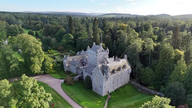 Elevated wide aerial drone video of 15th-century medieval Cawdor Castle featuring its stone tower house, surrounding woodland forest, and estate pathways near Nairn, Scottish Highlands, Scotland