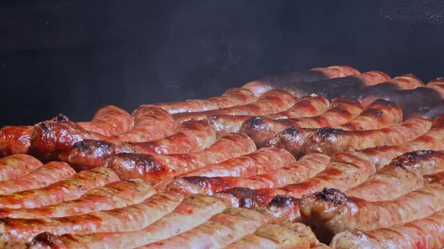 Slow zoom out of sizzling Argentine chorizo sausages grilling on outdoor parilla barbecue