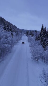 Aerial view car driving on snowy winter road through forest, Norway