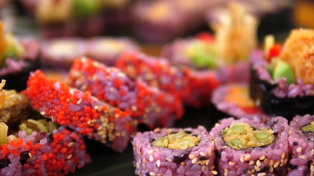 Sushi rolls rest in buffet display with bold pink rice, red roe, and crisp toppings, and sushi platter feels festive in japanese style. Sushi assortment is packed tightly in neat rows for serving.